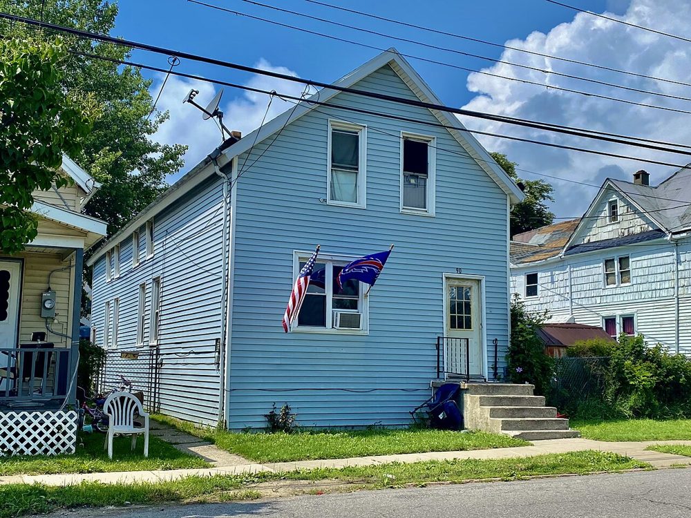 A light blue two-story wooden house on a street in Buffalo, New York